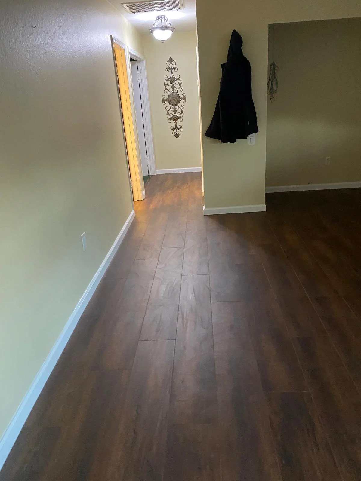Empty hallway with yellow walls, wood flooring, a coat hanging on the wall, decorative wall art, and a ceiling light fixture.