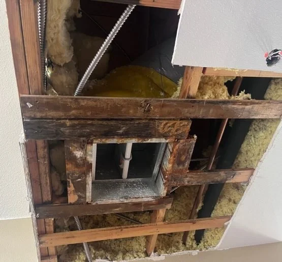 Open ceiling reveals wooden framing, insulation, plumbing pipes, and electrical wiring.