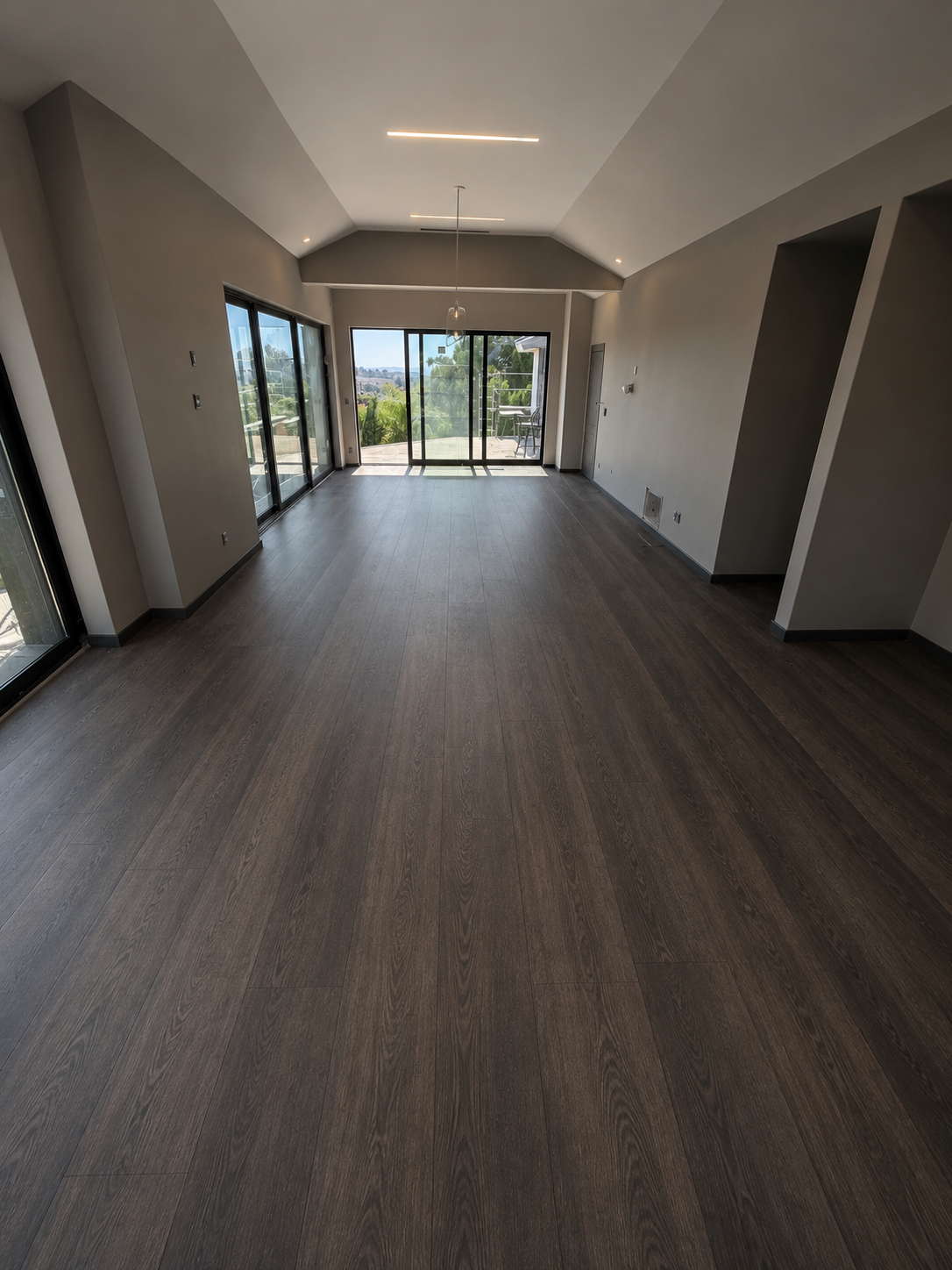 Empty living room with dark wood flooring, large sliding glass doors leading to outdoor patio, and neutral-colored walls.