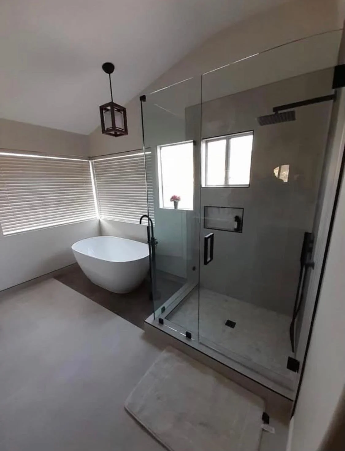 Modern bathroom with a freestanding bathtub by a window, a glass-enclosed shower, and horizontal blinds.