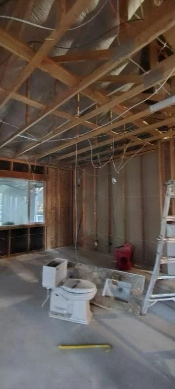 Construction site with exposed wooden beams, wiring, a ladder, and a toilet in the foreground.