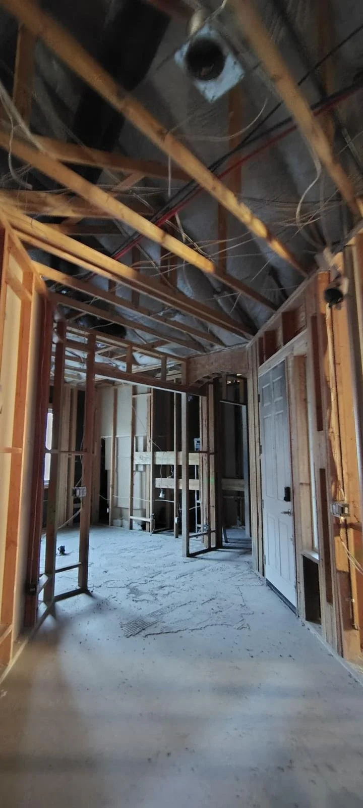 Interior of a house under construction with exposed wooden framing, wiring, and unfinished flooring.