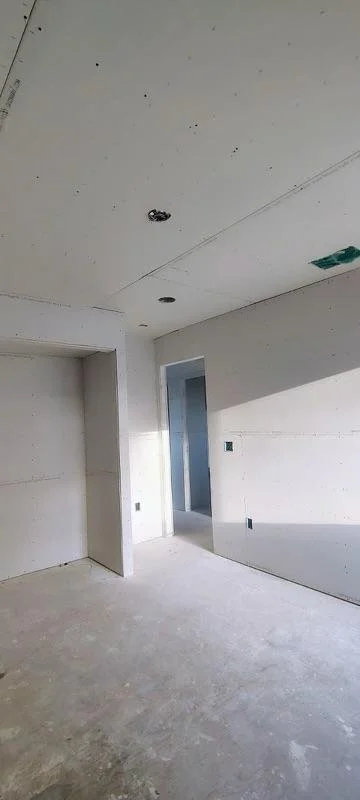 Empty room under construction with drywall, ceiling cutouts, and unfinished flooring.