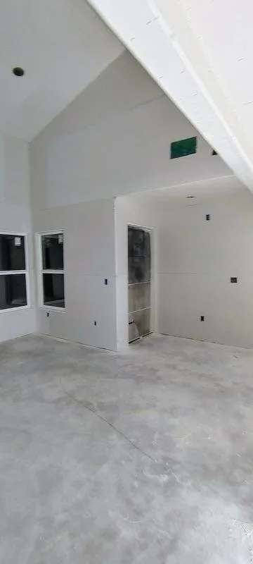 Interior of a room under construction with unfinished drywall, three windows, and an open doorway.