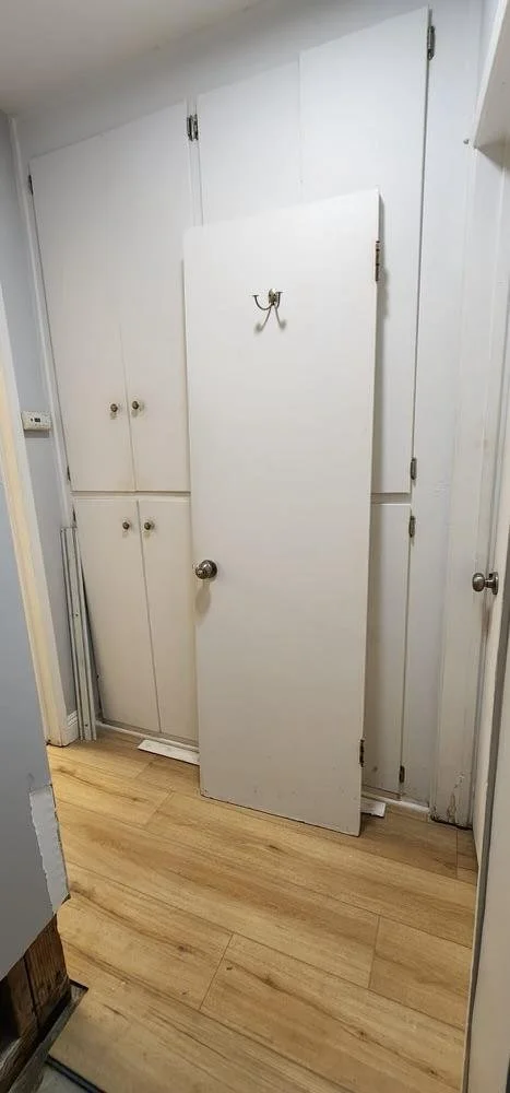 A partially open white door leaning against white built-in cabinets with round knobs, in a room with wooden flooring.