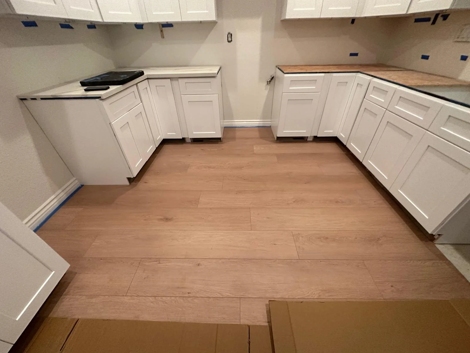 Empty kitchen with white cabinets, some with open shelves, hardwood flooring, and a partially installed countertop.