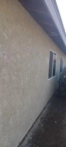 Exterior beige stucco wall with two small windows and grey roof overhang.