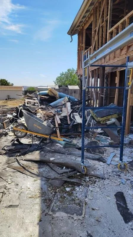 Construction site with debris, a wheelbarrow, and scaffolding next to a partially built wooden house.