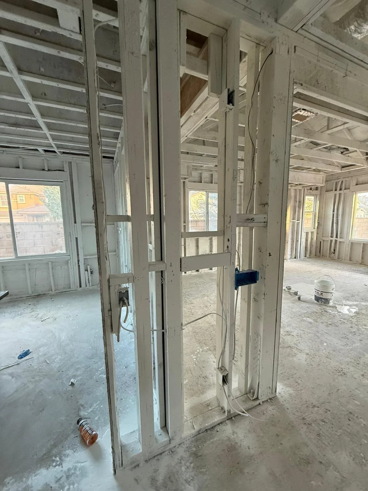Interior of a house under construction with exposed wooden framing, windows, and construction tools and materials on the floor.