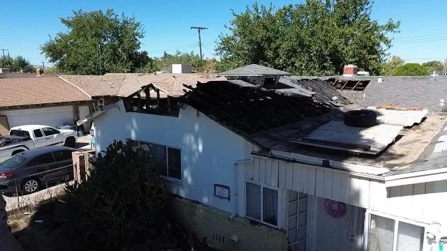 A house with severe fire damage to the roof, with charred and missing shingles, and burned sections visible on the upper part of the structure.