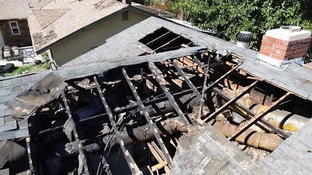 Damaged roof with missing shingles and exposed wooden beams, indicating significant fire damage.