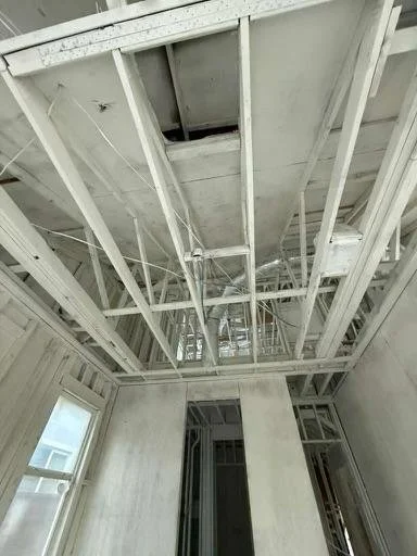 Construction site with exposed ceiling framing and open ceiling hatch, in a room with unfinished walls and windows.