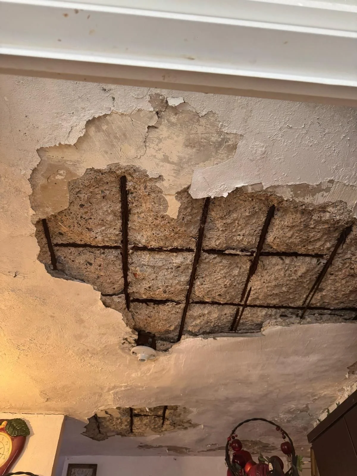Ceiling with exposed damaged and crumbling concrete and steel reinforcement bars.