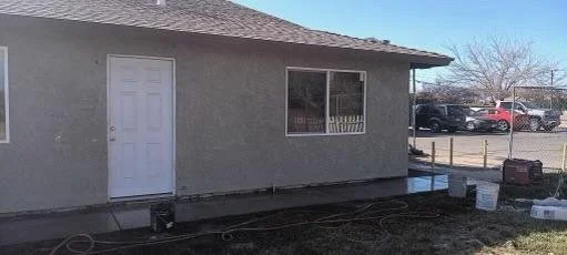 Exterior view of a house with a white door, a large window, and construction supplies outside on a sunny day.