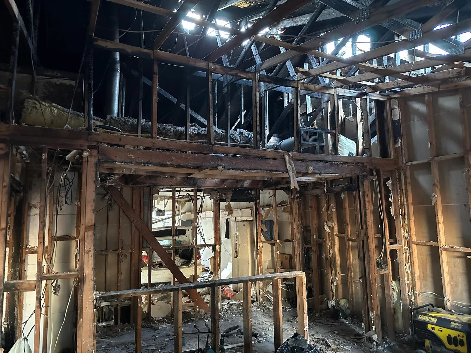 Under construction room with exposed wooden framing, wires, and debris, suggesting renovation or demolition work.