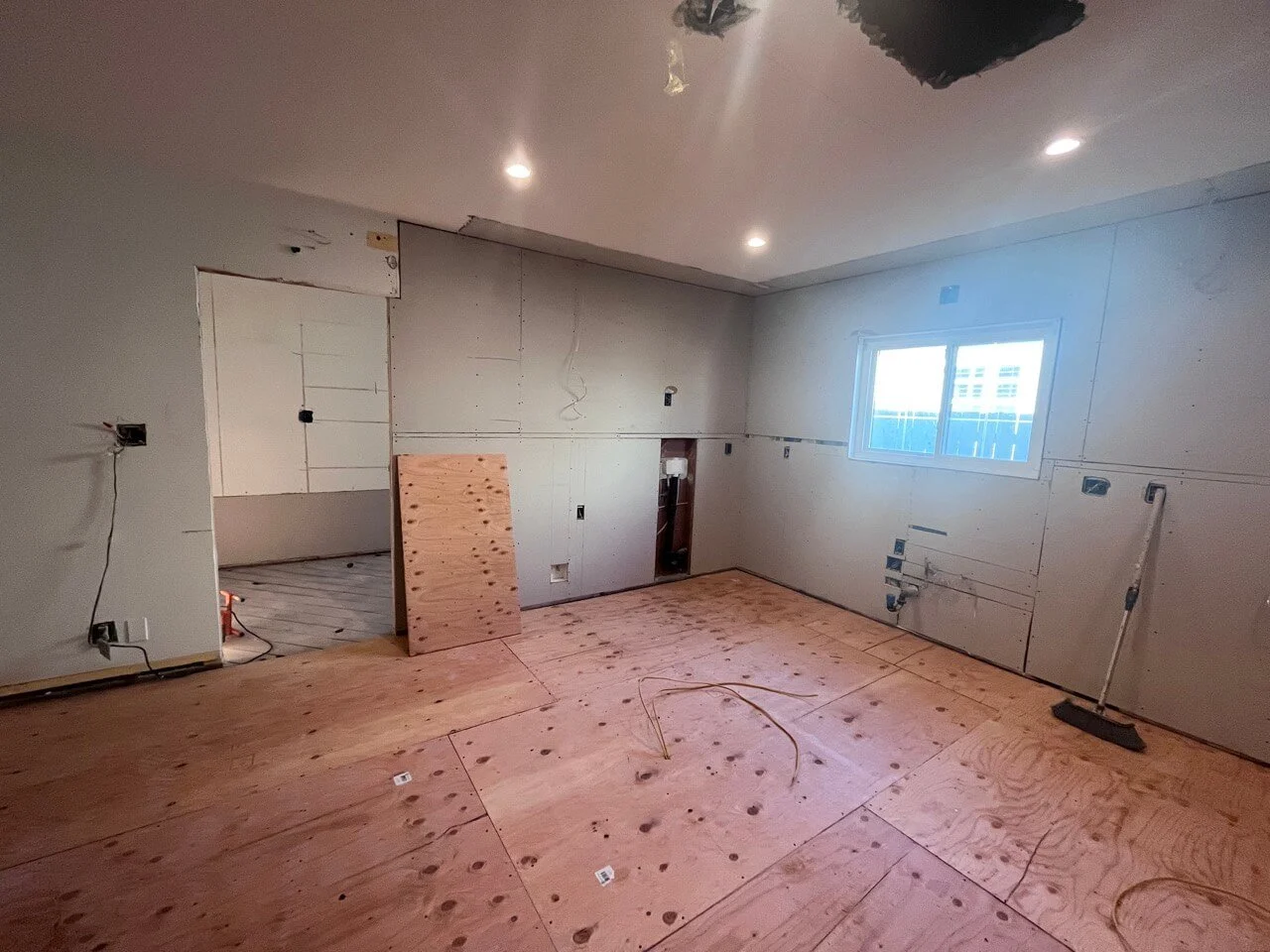 Room under construction with plywood flooring, unfinished drywall, electrical outlets, a window, and construction tools.