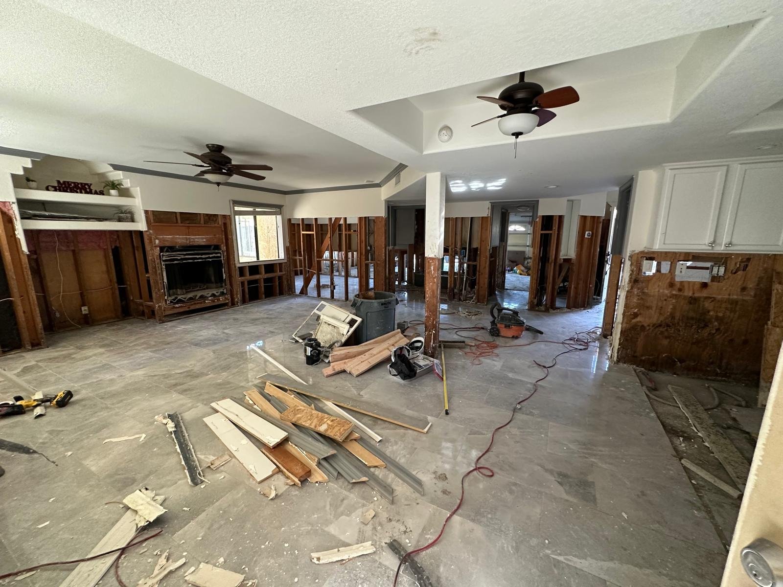 Living room under renovation with exposed wall studs, construction tools, and scattered debris on the floor.