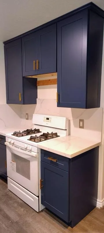 Kitchen with dark blue cabinets, white stove, marble countertop, and beige walls.