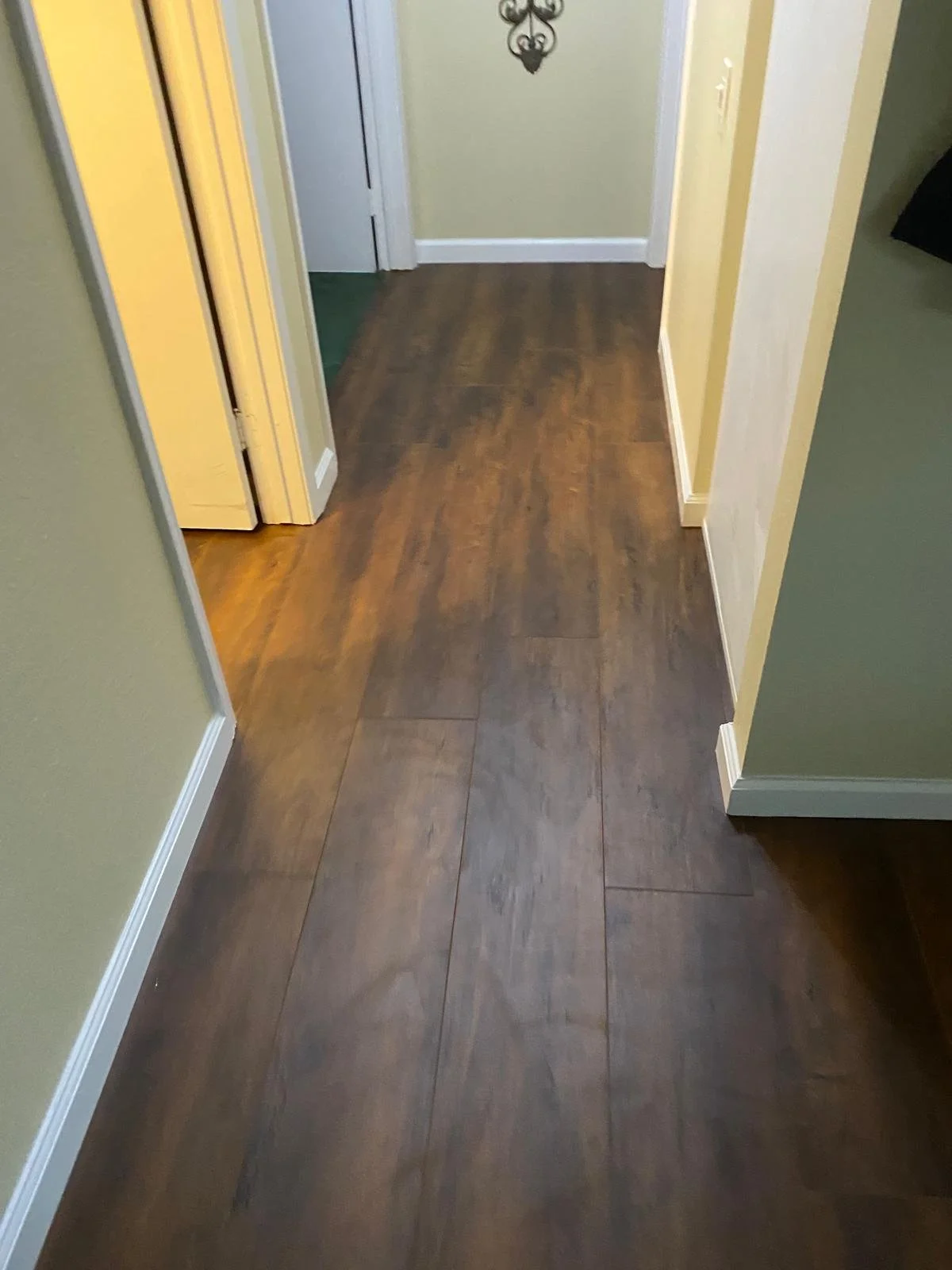 Photo of a hallway with dark wood flooring, beige walls, white baseboards, and a door at the end of the hall.