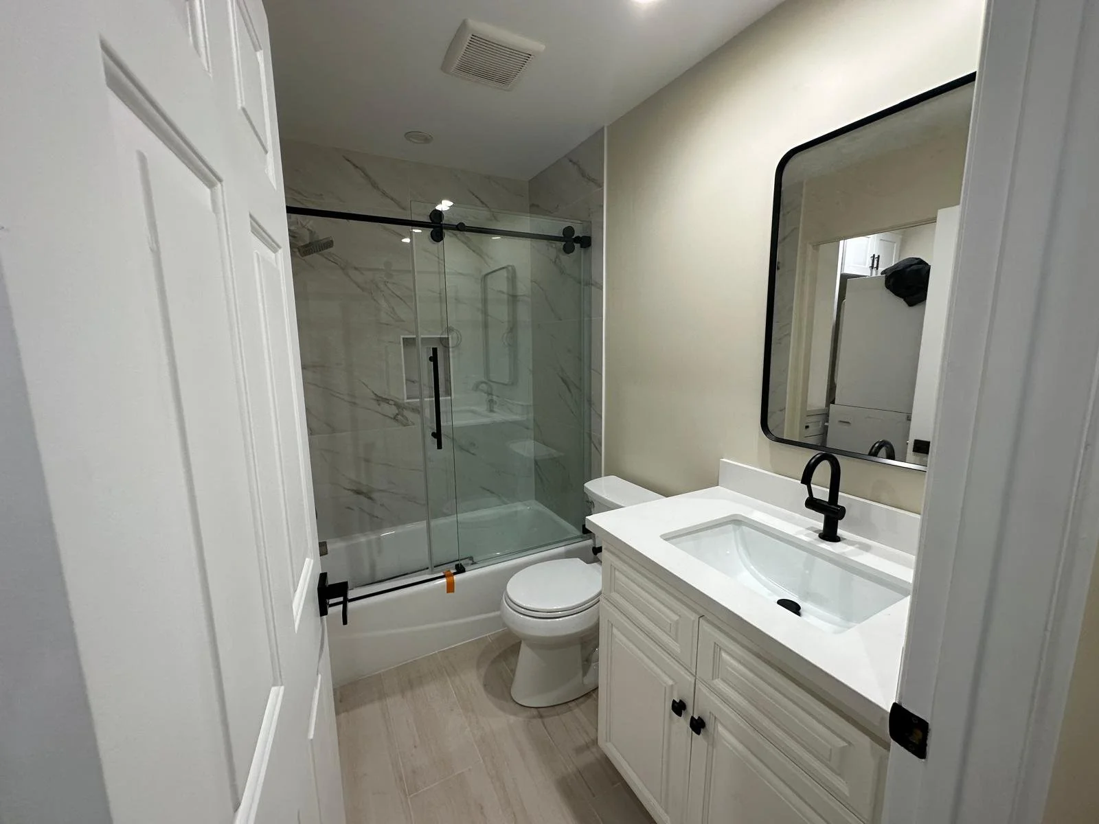 A bathroom with a white vanity, a mirror, a toilet, and a glass-enclosed shower with marble walls.