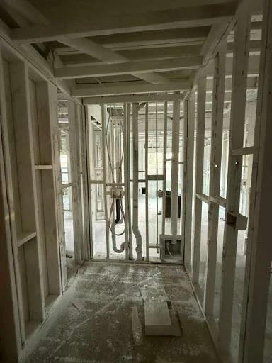 Interior view of a building under construction with exposed wooden framing and construction materials on the floor.
