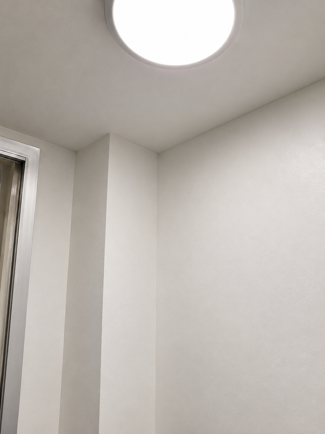 White ceiling with a round, bright ceiling light and corner of white walls with a door frame.