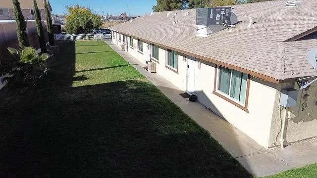 Side view of a single-story residential building with a concrete walkway, a well-maintained lawn, and an air conditioning unit outside.