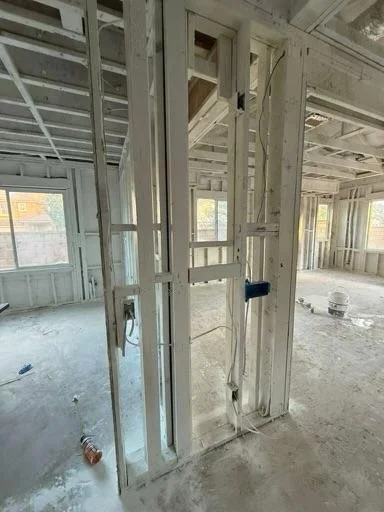 Interior of a building under construction with exposed wooden framing, electrical wiring, and unfinished walls.