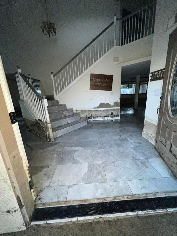 Interior of a building with tile flooring, a staircase with white railing, and walls with peeling paint and damage.