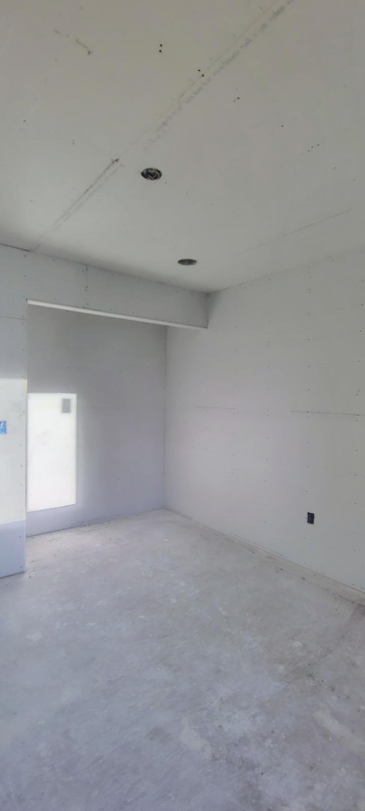 Unfinished room with white drywall, two ceiling light fixtures without bulbs, and an Earth-toned window letting in natural light.