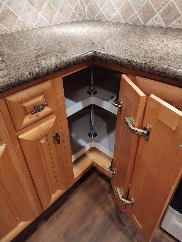 Open kitchen corner cabinet with dual hydraulic hinges, showing an empty interior with two shelves and the plumbing for a sink above.