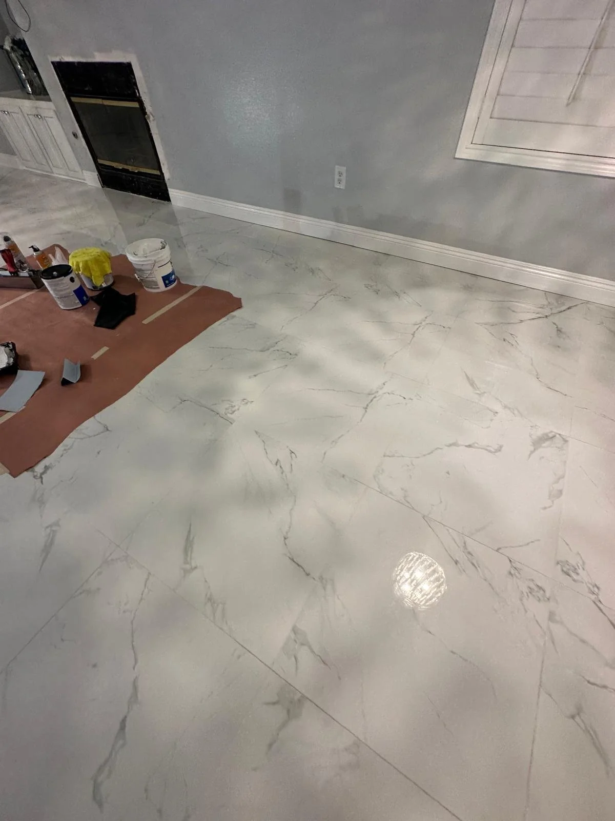 Marble-look white tile flooring in a room under renovation, with construction supplies nearby.