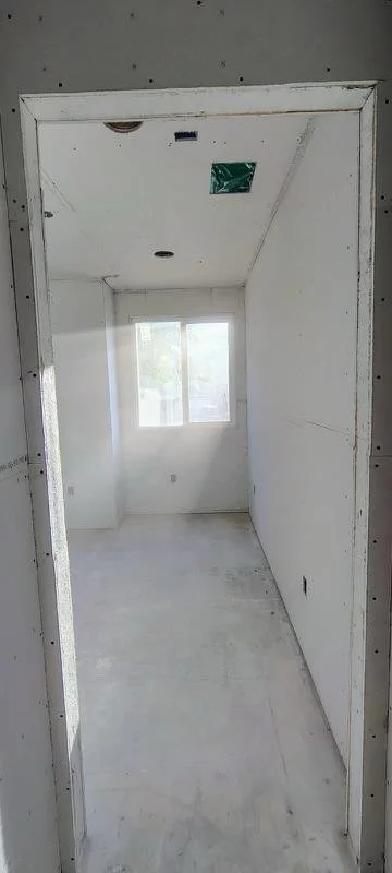 Empty room under construction with a window, white drywall, and unfinished walls.