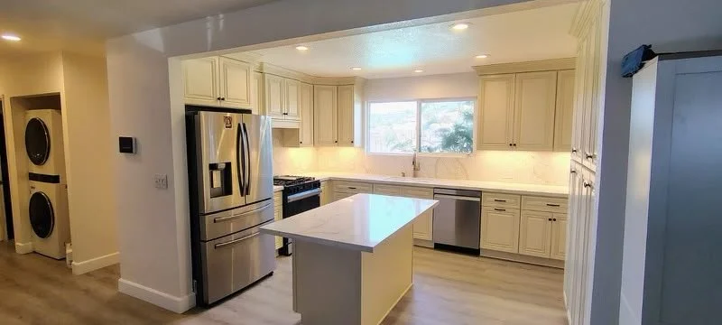 Kitchen with white cabinets, marble island, stainless steel refrigerator, gas stove, dishwasher, and a window over the sink.