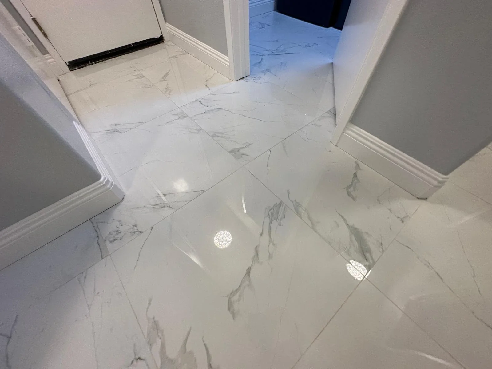 Marble tile flooring in a hallway with a door at the end and gray walls.