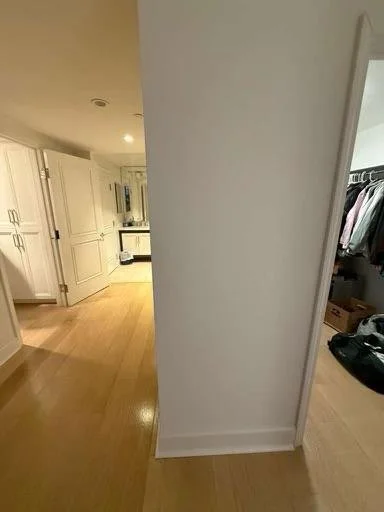 View of a beige-colored kitchen and a walk-in closet with hanging clothes, seen from around a corner in a home interior.