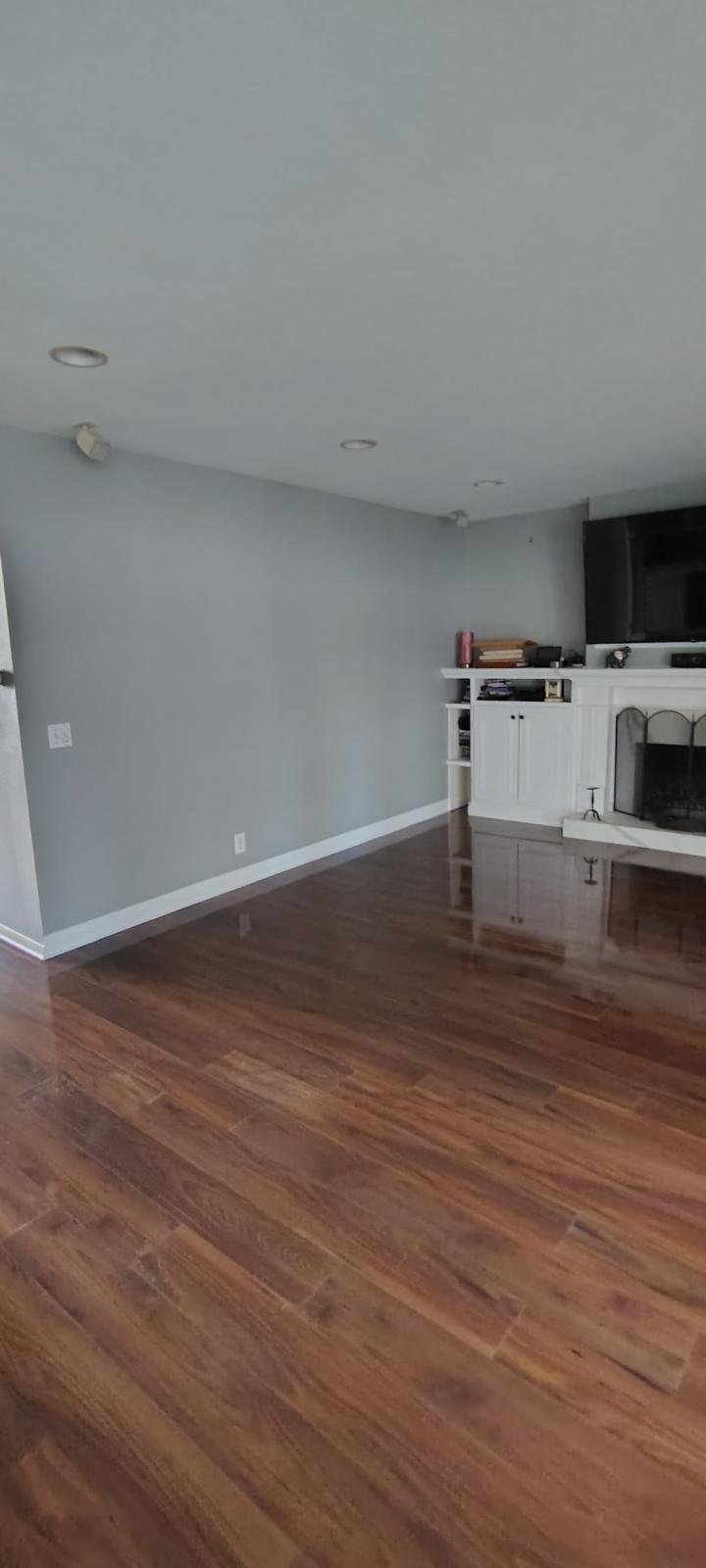 Empty living room with hardwood floors, gray walls, and a white fireplace with built-in shelving. Minimal furniture and decor.