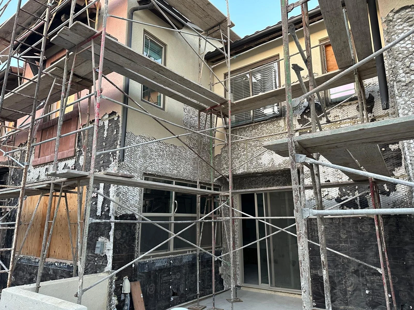 Construction scaffolding surrounds a building under renovation, with exposed walls and windows visible.