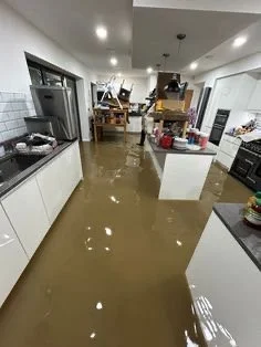 Flooded kitchen with brown water covering the floor, cluttered countertops, and scattered items.