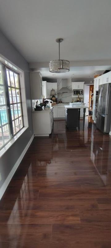Bright kitchen with white cabinets, stainless steel appliances, and hardwood floors, viewed from an adjacent room with large windows.