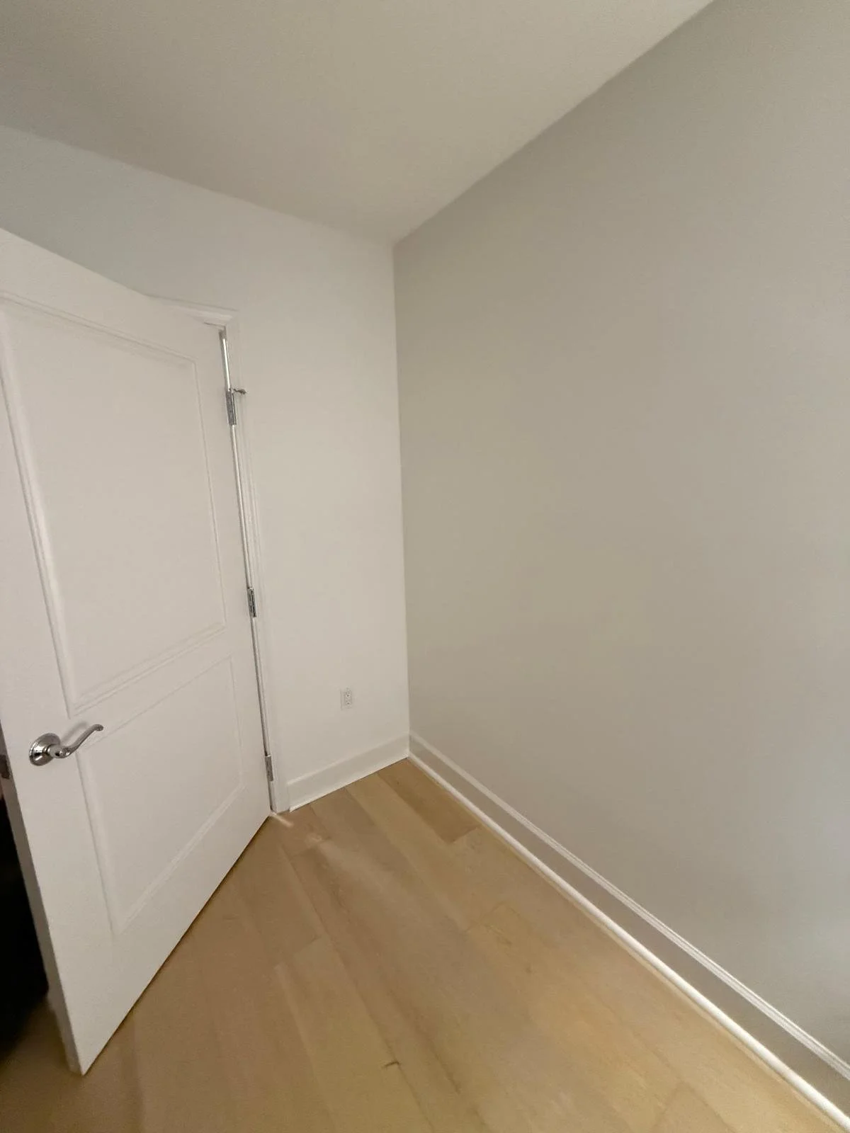 Empty room with white walls, a closed white door with a silver handle, and light wooden flooring.