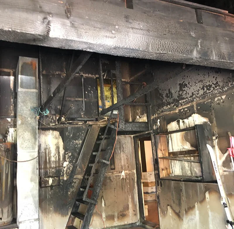 Interior of a building severely damaged by fire, showing burned walls, charred stairs, and smoke damage.