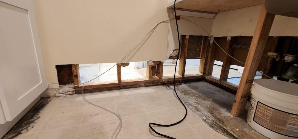 Kitchen with a large hole in the wall beneath the cabinet, exposing the wooden framing and electrical wiring.