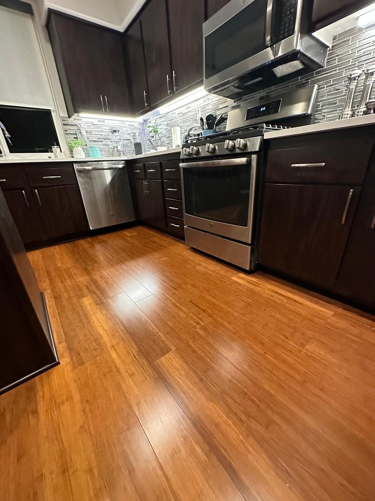 Modern kitchen with dark wood cabinets, stainless steel appliances including microwave and stove, gray tile backsplash, and hardwood flooring.