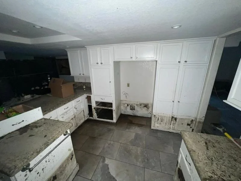 Kitchen with white cabinets and granite countertops, showing stained and damaged lower cabinets and floor from a leak or water damage.
