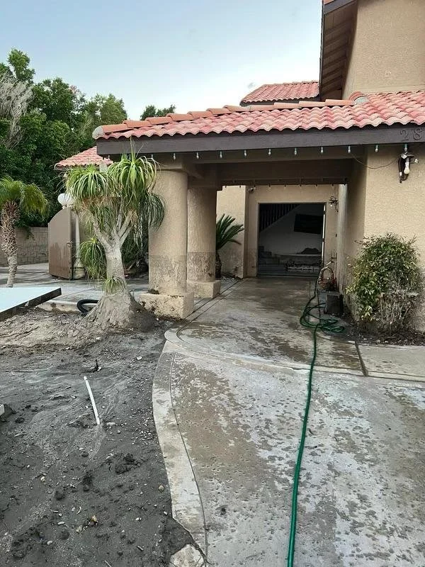 Front view of a house with a concrete porch, garden hose on the ground, and a landscaped yard with trees and bushes.