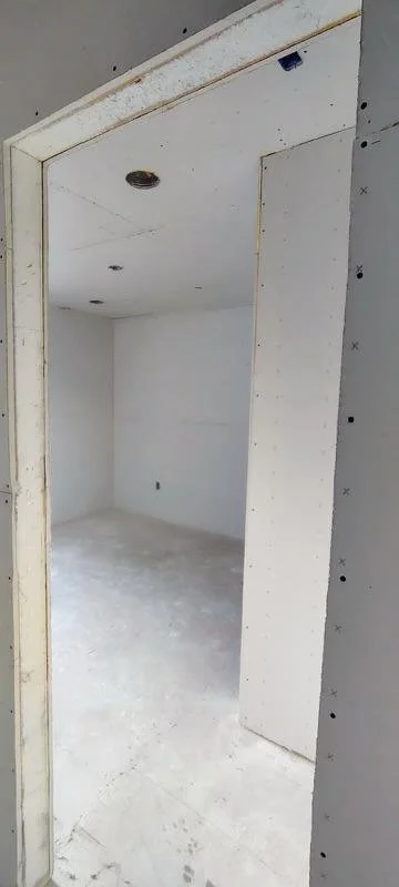 Empty room under construction with white drywall, unfinished flooring, and an open doorway.