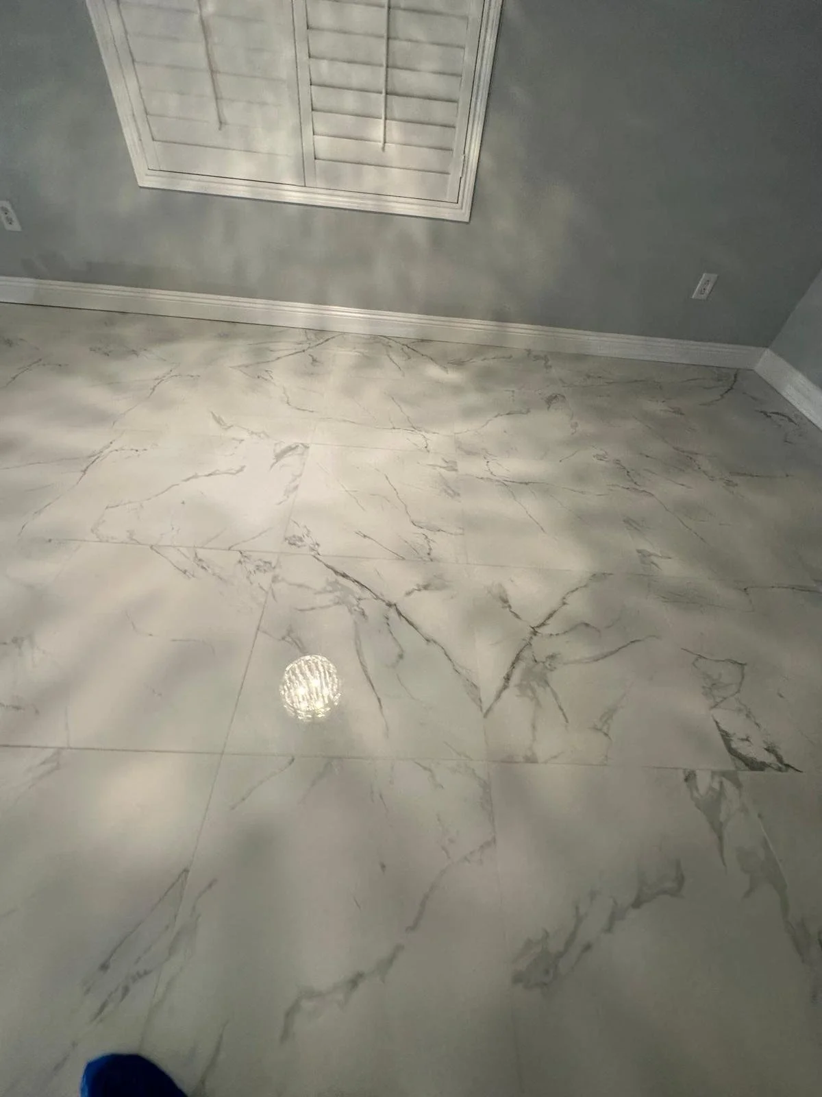 Interior room with shiny marble floor and gray walls, a window with closed white shutters, and electrical outlets on the walls.
