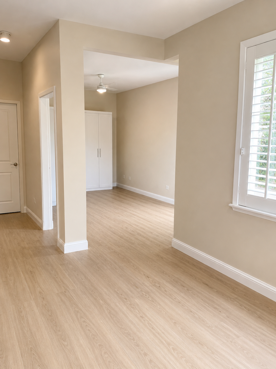 Empty room with beige walls, hardwood floors, a window with shutters, and a white ceiling fan.