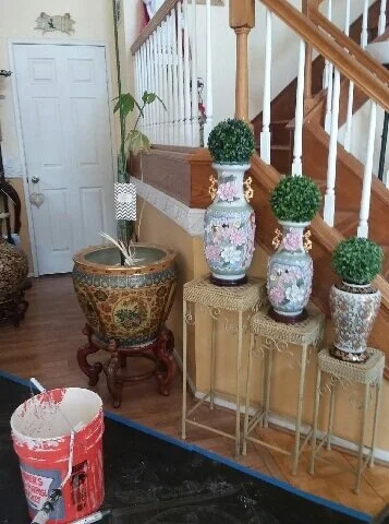 Decorative plants and vases on small tables near staircase in a home interior.